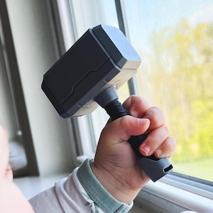 This 3D printed Thor hammer baby rattle features a personalized name engraving and colorful handle options like pink, blue, black, brown, and yellow. A fun and durable custom baby gift that doubles as a playful 3D printed toy.