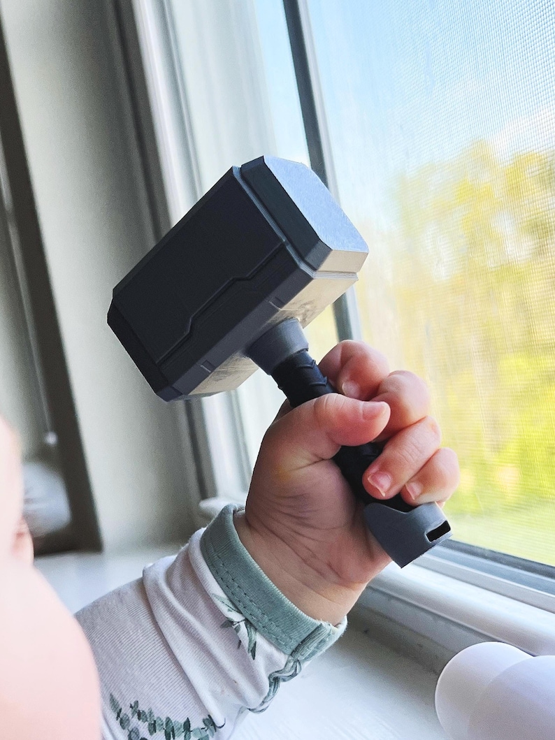 This 3D printed Thor hammer baby rattle features a personalized name engraving and colorful handle options like pink, blue, black, brown, and yellow. A fun and durable custom baby gift that doubles as a playful 3D printed toy.