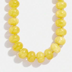 May include: A necklace composed of light yellow, oval-shaped beads. The beads are strung together, creating a curved shape against a white background. The necklace is a simple, elegant piece of jewelry.