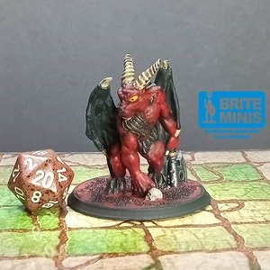 May include: A red miniature demon figure with black wings, horns, and a skull at its feet. The figure is on a round base. A twenty-sided die is in the foreground. The text "BRITE MINIS" is in the background.