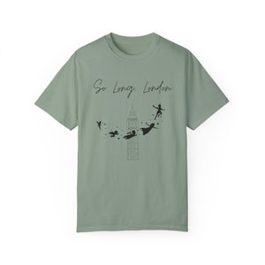 May include: A sage green t-shirt with a black graphic of Big Ben and Peter Pan characters flying away. The text "So Long, London" is printed on the shirt.