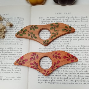 Puede incluir: Dos lupas de madera con intrincados dise&ntilde;os florales. La lupa superior tiene hojas verdes y la lupa inferior tiene hojas rojas. Las lupas est&aacute;n sobre un libro con texto.