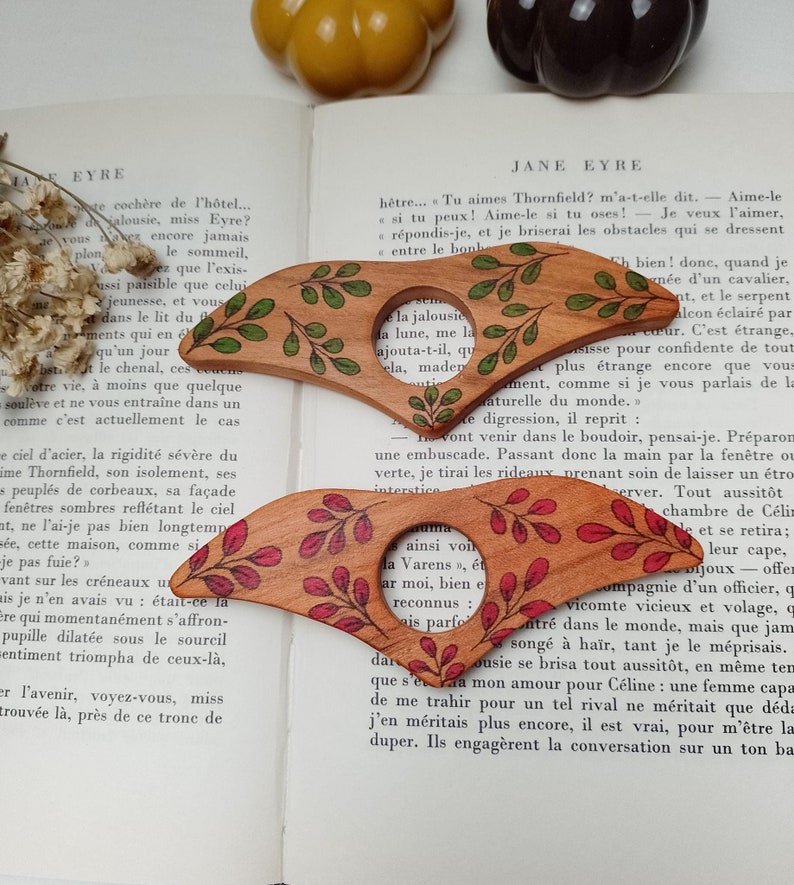 Puede incluir: Dos lupas de madera con intrincados dise&ntilde;os florales. La lupa superior tiene hojas verdes y la lupa inferior tiene hojas rojas. Las lupas est&aacute;n sobre un libro con texto.