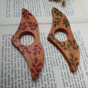 Puede incluir: Dos marcap&aacute;ginas de madera con un dise&ntilde;o de hojas. Uno est&aacute; pintado con hojas verdes y el otro con hojas rojas.