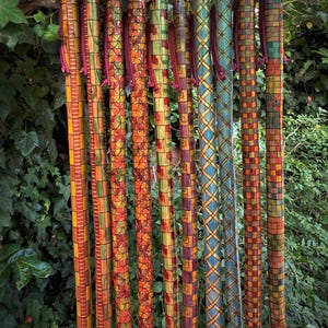 Pode incluir: Uma coleção de dez bengalas decorativas, cada uma com padrões geométricos únicos e coloridos. As bengalas apresentam uma variedade de desenhos, incluindo quadrados, linhas e motivos florais, em tons de vermelho, laranja, verde e azul. Cada bengala tem uma correia de couro.
