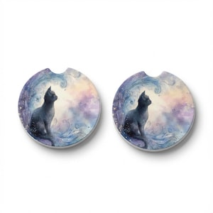 May include: Two round car coasters featuring a watercolor illustration of a black cat. The cat is seated, gazing upwards, surrounded by swirling blue and purple waves and a pastel sky. The coasters have a small notch for easy removal.