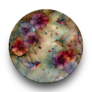 May include: Round decorative plate featuring a watercolor design of hummingbirds and flowers. The plate has a soft, muted color palette with shades of red, purple, and green. The hummingbirds are depicted in flight, adding a sense of movement.
