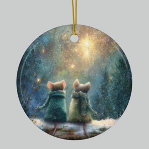 Może przedstawiać: Okrągła ozdoba świąteczna przedstawiająca dwie myszy w zielonych swetrach patrzące na jasną gwiazdę na gwiaździstym niebie. Ozdoba ma złoty sznurek do zawieszenia i zimową scenę leśną.