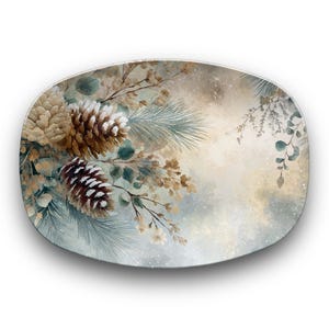 May include: Oval decorative plate with a winter theme. The plate features a watercolor design of pine cones, pine needles, and other foliage in shades of brown, beige, and blue-green. The background has a soft, blurred effect.