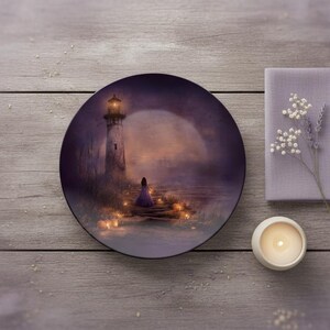 May include: A decorative plate with a lighthouse scene in shades of purple and orange. A figure in a long dress stands near the lighthouse. A lavender napkin, flowers, and a candle are also present.