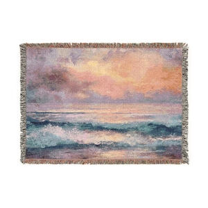 May include: Woven throw blanket featuring an ocean scene with a sunset. The artwork depicts waves in shades of blue and turquoise, with a sky of pink, orange, and purple hues. The blanket has a fringed edge.