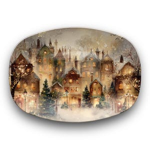 May include: Oval decorative plate with a watercolour painting of a snow-covered village at dusk. The artwork depicts buildings with lit windows, Christmas trees, and falling snow, creating a cosy winter scene.