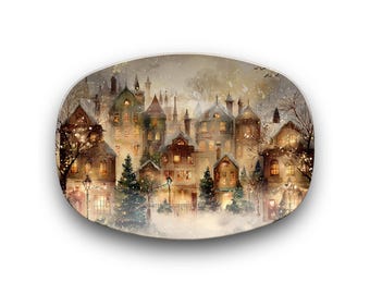 Può includere: Piatto decorativo ovale con un dipinto ad acquerello di un villaggio innevato al crepuscolo. L'opera raffigura edifici con finestre illuminate, alberi di Natale e neve che cade, creando una scena invernale accogliente.