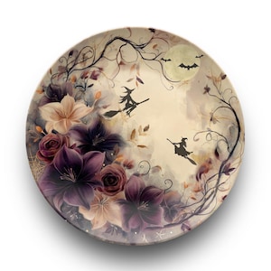 Puede incluir: Plato decorativo redondo con temática de Halloween. El plato presenta un diseño floral con flores moradas y crema, siluetas de brujas en escobas, una luna llena y murciélagos.