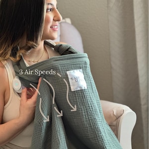 May include: A sage green baby carrier with the text "3 Air Speeds" and a white label that says "LADY ALPHA". The carrier is made of a soft, textured fabric and appears to be designed for comfort.