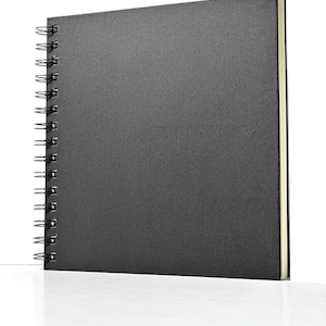 May include: A black spiral bound sketchbook with a textured cover. The cover is made of a fabric-like material.