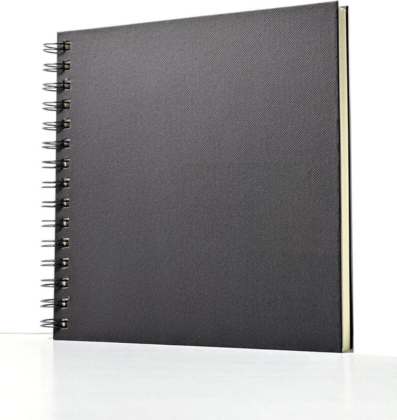 May include: A black spiral bound sketchbook with a textured cover. The cover is made of a fabric-like material.