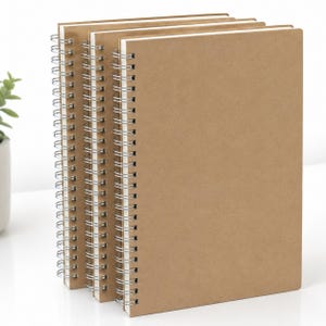 May include: A pile of spiral-bound notebooks with kraft paper covers. The notebooks have a silver metal spiral binding and white paper pages. The covers are a light brown colour. The notebooks are stacked together.