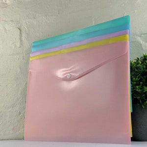 May include: A set of four pastel-coloured plastic folders with a snap closure. The folders are stacked on top of each other, with the top folder being pink, the next folder being yellow, the next folder being light blue, and the bottom folder being a darker blue.