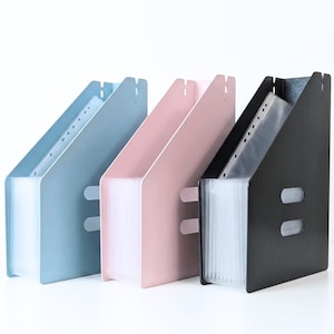 May include: Three expanding file organisers in pastel shades: light blue, pink, and black. Each organiser has a slanted design with clear, plastic pockets. The files are designed to hold documents and papers, suitable for office or school use.
