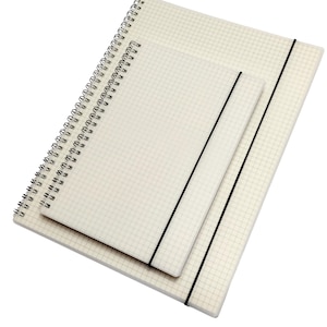 May include: Three notebooks of different sizes, stacked. The notebooks have a grid pattern on the pages and either a spiral binding or an elastic band closure. The covers are off-white.