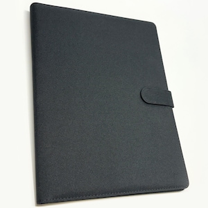 May include: A rectangular black portfolio folder with a textured surface and a matching black strap closure on the right side. The folder is closed and features clean, stitched edges along the perimeter, providing a structured and uniform appearance.