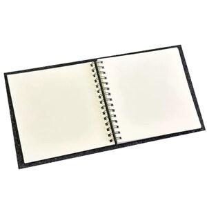 May include: A black spiral bound notebook with a soft, textured cover. The notebook is open to a blank page.