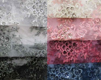 May include: Close-up of several fabric swatches with floral lace patterns. The fabrics are in various colors, including white, gray, pink, and navy blue. Each swatch is embellished with sequins, adding a shimmering effect to the delicate designs.