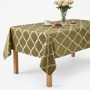 May include: Olive green tablecloth with a cream-colored geometric pattern. The rectangular tablecloth is draped over a wooden table, with a vase of pink roses, a teacup, and small plates of berries on top.