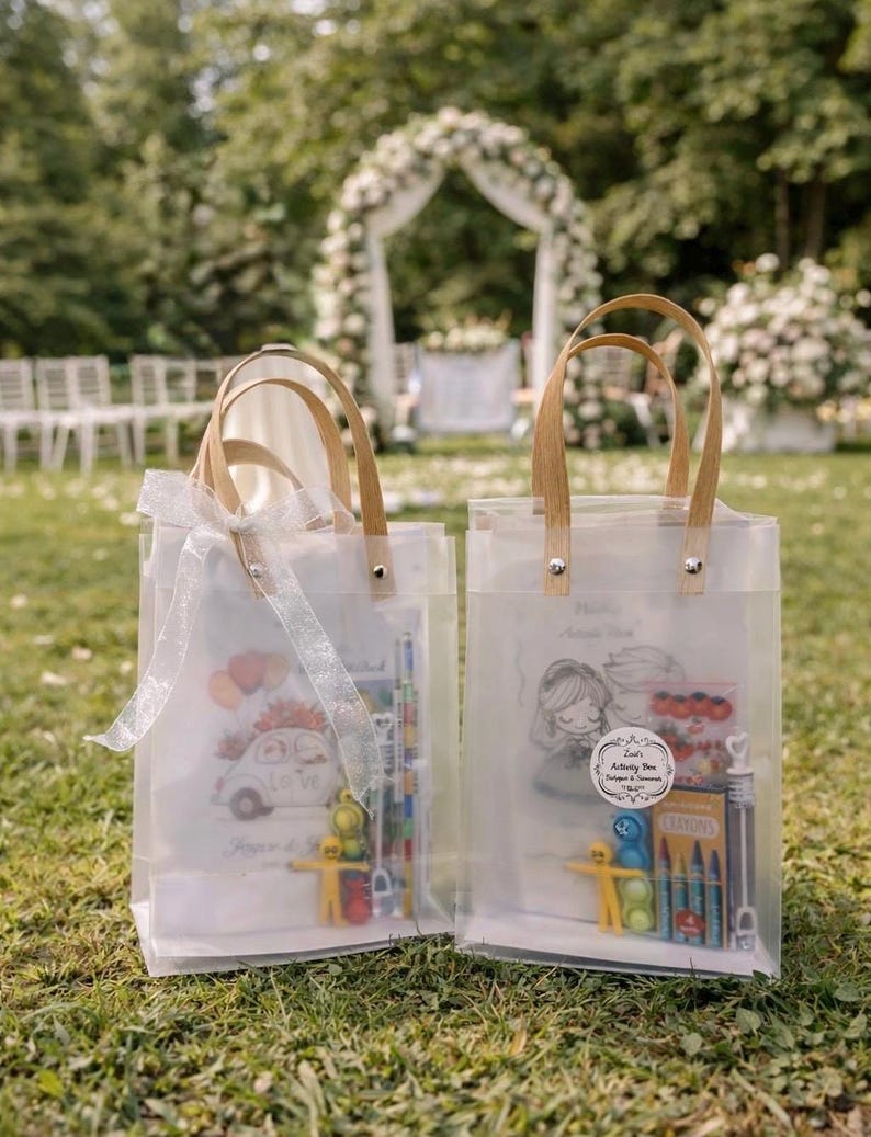 May include: Two clear tote bags with wooden handles and illustrations. One bag features a car with flowers and the text "Love". The other bag has a drawing of a couple and the text "Activity Box". Both bags contain crayons and toys.