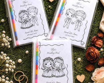 May include: Three rectangular wedding activity packs in clear plastic sleeves, each featuring a black and white cartoon illustration, the text "Theo's Wedding Pack", "Sarah & James", "26th March 2024", and a multi-coloured stacking crayon pencil.