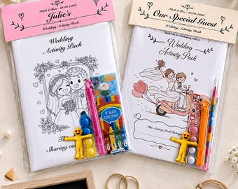 May include: Two wedding activity packs in clear plastic packaging with pink and beige headers. Each pack includes a colouring book, four wax crayons, and a yellow emoji-style fidget toy. The covers feature illustrations of a bride and groom.