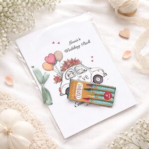 May include: A wedding pack with a cartoon illustration of a car carrying a bride and groom, balloons, and flowers. The pack includes a small box of crayons. The text on the pack reads "Lewis's Wedding Pack".