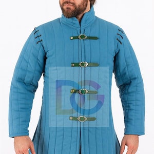 Peut inclure: Une tunique matelassée bleu clair avec un col montant et des sangles en cuir vert. La tunique présente des coutures verticales et est fermée par trois boucles décoratives. Les manches sont longues et le vêtement semble être fait d'un tissu épais et durable.