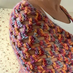 Pu&ograve; includere: Uno scialle all'uncinetto fatto a mano, a trama aperta, in una miscela di colori tra cui viola, arancione, grigio e giallo. Lo scialle &egrave; drappeggiato sulle spalle, mettendo in mostra il motivo a punto strutturato e la miscela di toni caldi e freddi. Il filato sembra essere di un peso morbido e voluminoso.