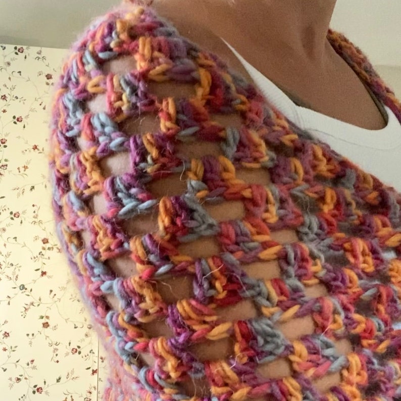 Pu&ograve; includere: Uno scialle all'uncinetto fatto a mano, a trama aperta, in una miscela di colori tra cui viola, arancione, grigio e giallo. Lo scialle &egrave; drappeggiato sulle spalle, mettendo in mostra il motivo a punto strutturato e la miscela di toni caldi e freddi. Il filato sembra essere di un peso morbido e voluminoso.