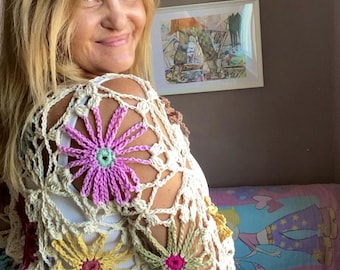 Può includere: Un top bianco all'uncinetto con dettagli floreali colorati. Il top ha un design sciolto a trama aperta e presenta una varietà di colori, tra cui rosa, giallo e verde.