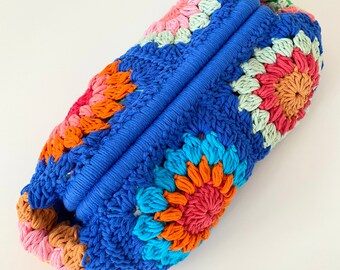Può includere: Una borsa di uncinetto blu con motivi floreali colorati in tonalità di rosa, arancio, verde e turchese.