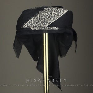 Könnte beinhalten: Ein schwarzer Turban mit weißem Paisley-Muster. Der Turban wird auf einem goldenen Ständer vor grauem Hintergrund präsentiert. Der Text "HISAR ABSTY" und "ROYAL CULTURE OF ELEGANCE & FASHION BRAND FROM THE UK." ist im Bild enthalten.