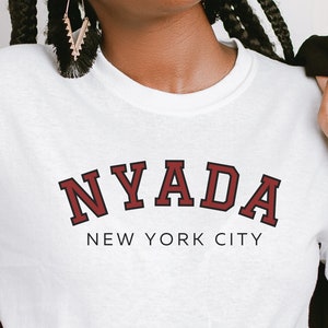 May include: White t-shirt with a red and black graphic that says "NYADA NEW YORK CITY"