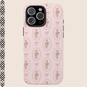 May include: A pink phone case with a repeating pattern of a nutcracker doll in a pink oval frame with a pink bow.