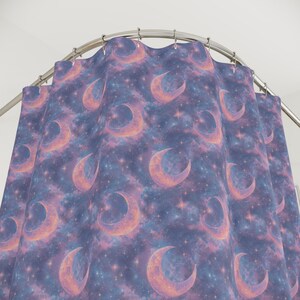 May include: A shower curtain with a celestial design. It features crescent moons and stars set against a purple and pink nebula background. The curtain hangs from a curved metal rail.