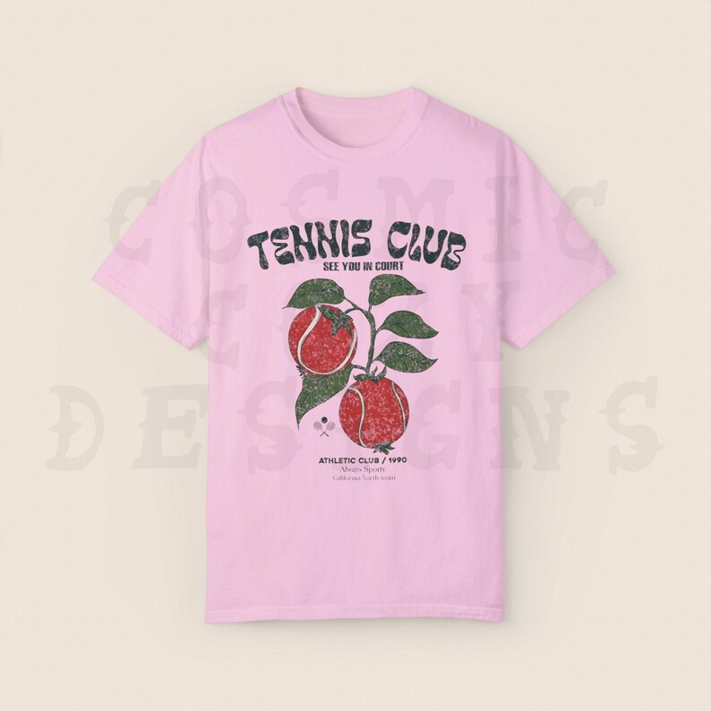 May include: Pink t-shirt with a vintage tennis club graphic. The graphic features a tennis racket, two tennis balls, and the text "Tennis Club See You In Court Athletic Club / 1990"