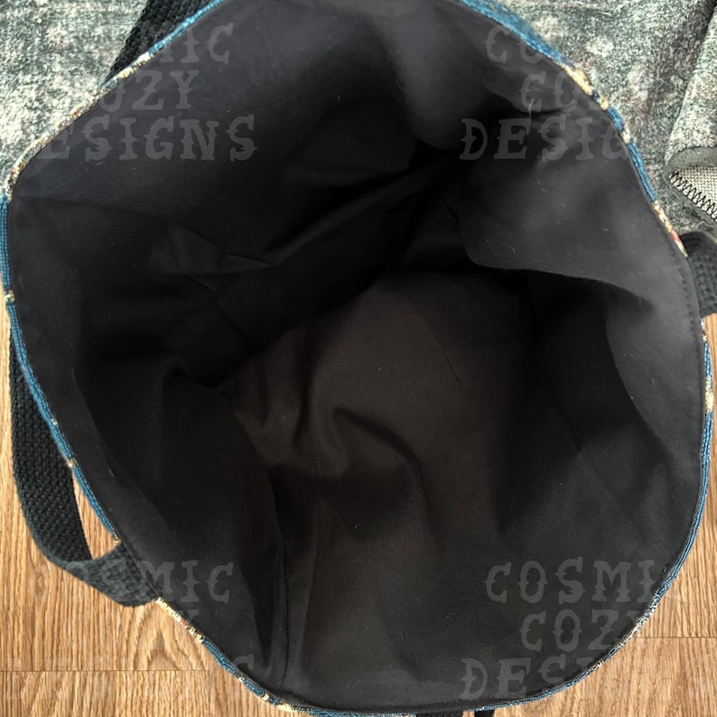 Pu&ograve; includere: Vista aperta di una borsa tote con interno nero ed esterno fantasia. La borsa ha un cinturino nero e le parole "COSMIC COZY DESIGNS" sono visibili sul lato.
