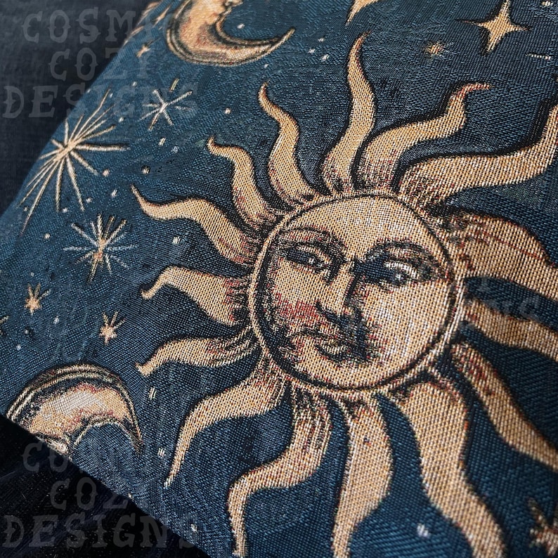 May include: A decorative pillow with a celestial design. The pillow features a detailed illustration of a sun with a face, surrounded by stars and crescent moons, set against a dark blue background. The pillow has a textured appearance.