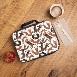 May include: A white lunch bag with a black zipper and handle. The bag is covered in a pattern of brown and black dachshund dogs in various poses.