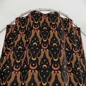 Könnte beinhalten: Schwarzer Duschvorhang mit einem sich wiederholenden Muster aus stilisierten Geparden, Monden und Sternen in Orange, Gold und Weiß. Der Vorhang hängt an einer gebogenen Metallstange.