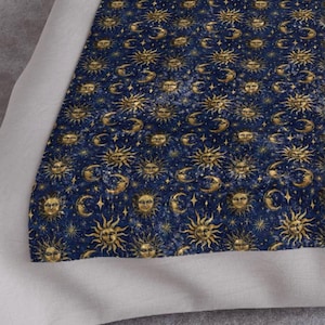 May include: A blue fabric with a repeating pattern of gold suns and moons. The suns and moons are surrounded by gold stars.