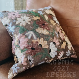 May include: A brown throw pillow with a floral pattern featuring pink, white, and red flowers. The pillow has a textured fabric and a subtle sheen.