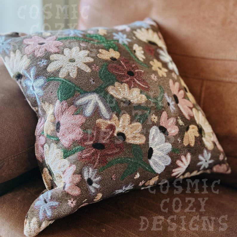 May include: A brown throw pillow with a floral pattern featuring pink, white, and red flowers. The pillow has a textured fabric and a subtle sheen.